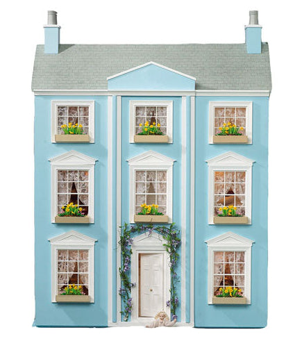 A miniature three-story dollhouse house with light blue walls, a gray roof, white trim, and tiny windows with green plants, centered on a plain white background.