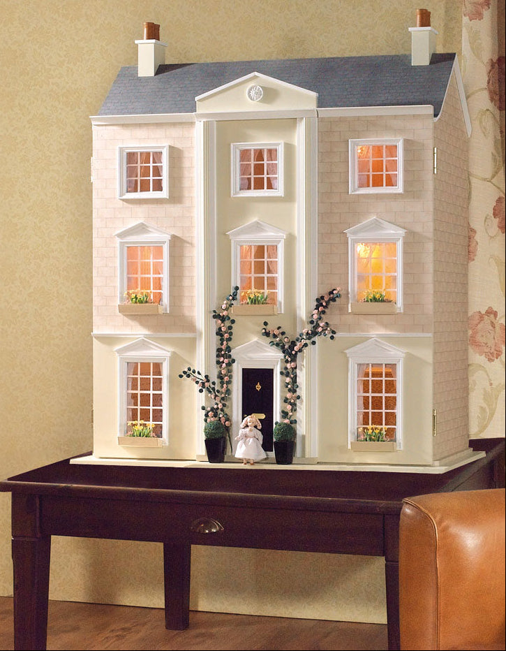 Model of a two-story house with lit windows on a wooden table against a beige wall.