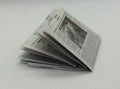 A miniature folded newspaper model, likely for dollhouse or scale modeling, placed on a white surface .