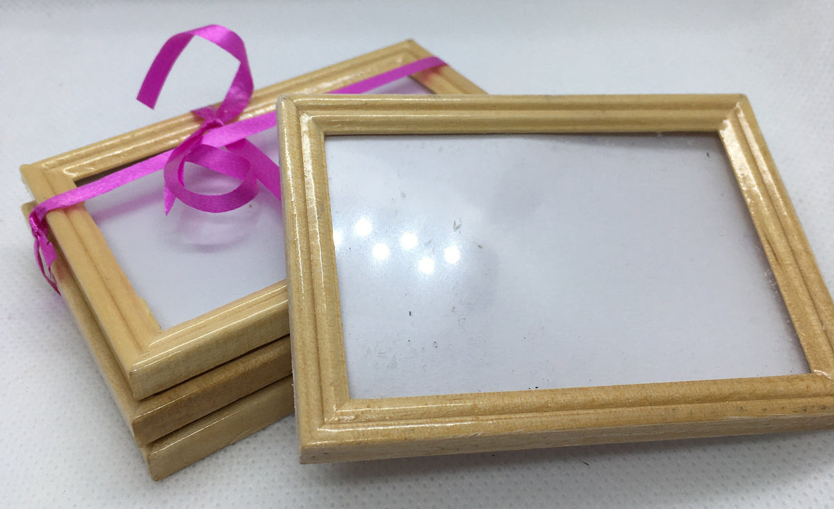 Four small rectangular picture frames with light wood borders and clear glass, tied together with a bright pink ribbon on a white textured fabric background.