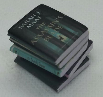 A small stack of miniature books likely dollhouse or scale model books, on a plain light gray textured background.