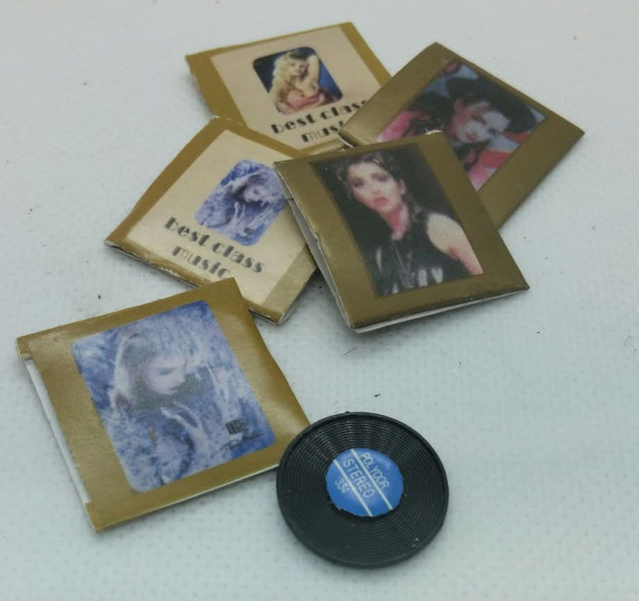 A set of miniature collectible items, including five small photo cards with gold borders and a small black vinyl record with a blue center label, arranged on a light gray textured surface.