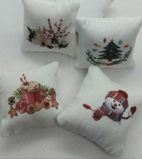 Four small white decorative pillows with embroidered Christmas designs, including a hot cocoa mug, a Christmas tree, berries, and a snowman, arranged on a white textured fabric background.