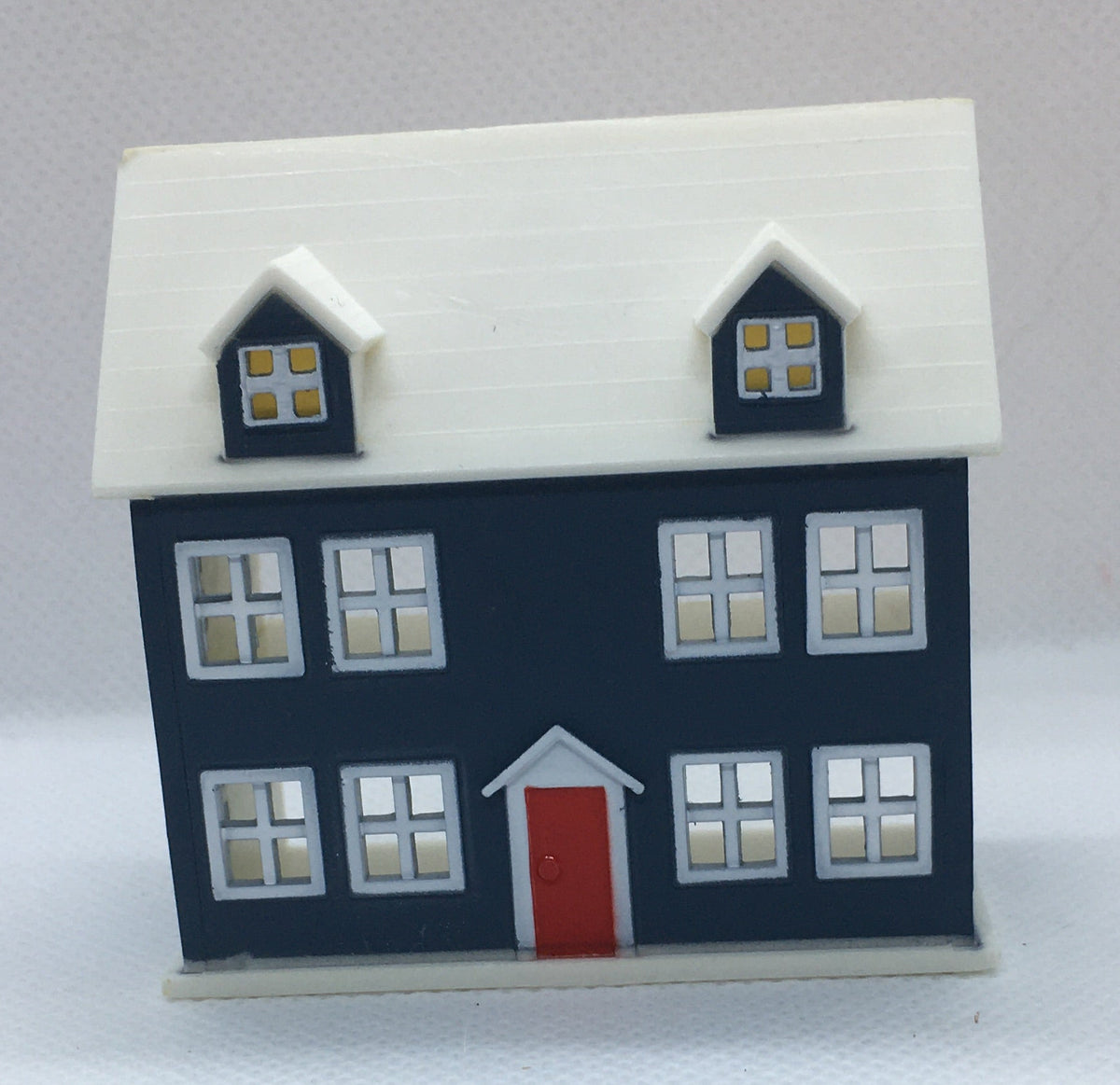 A miniature two-story house figurine with a dark navy blue body, a white roof, a red front door, and white-framed windows, set against a plain white background.