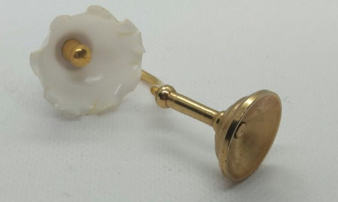 A single brass dolls house lamp with a white flower-shaped lampshade  and a gold stand, photographed on a white surface.