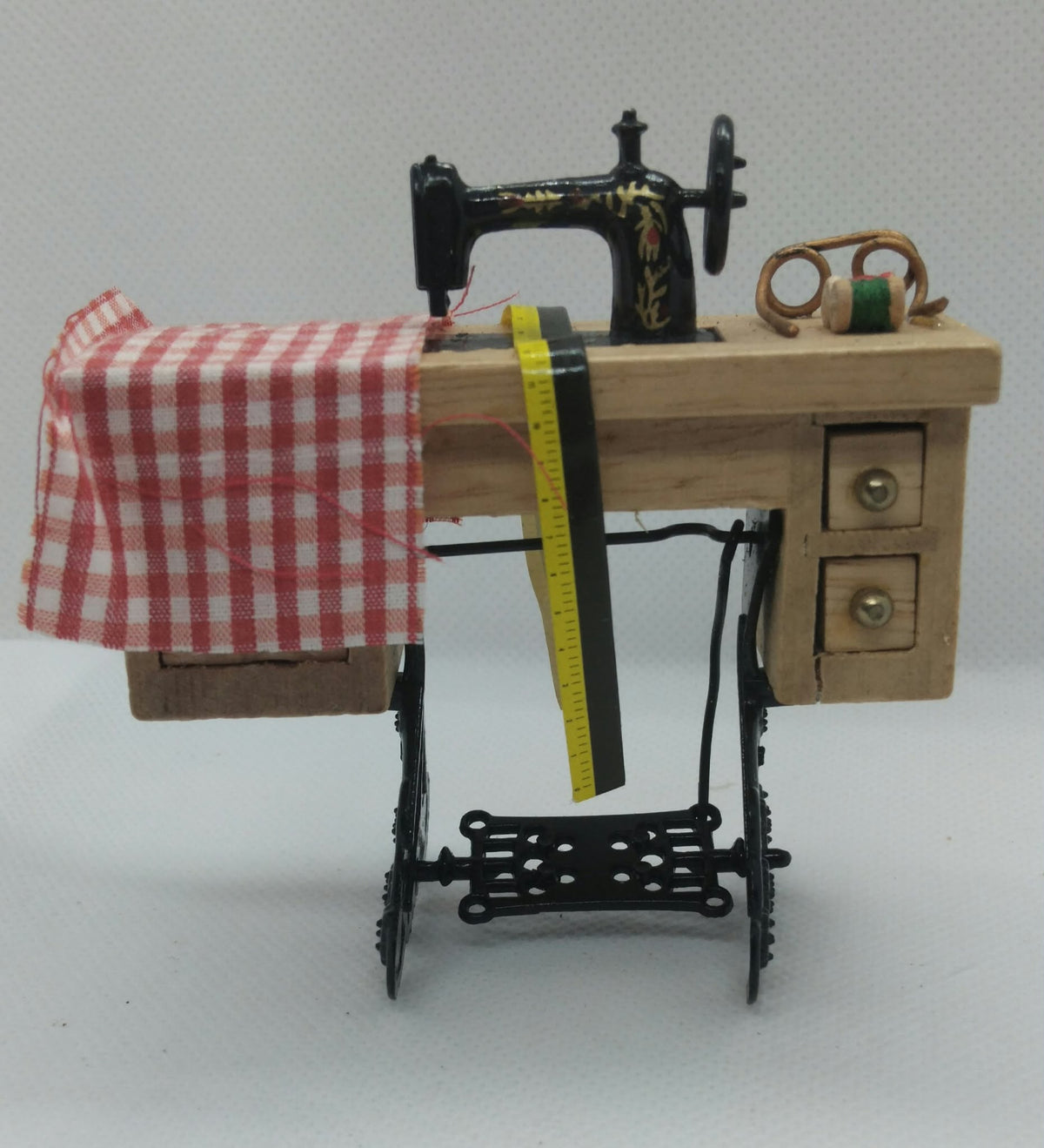 A miniature sewing machine dollhouse scale 1:12th model with a light wood body, black metal frame, red and white gingham fabric, a yellow measuring tape, and a spool of thread on a neutral background.
With a pair of spectacles. 