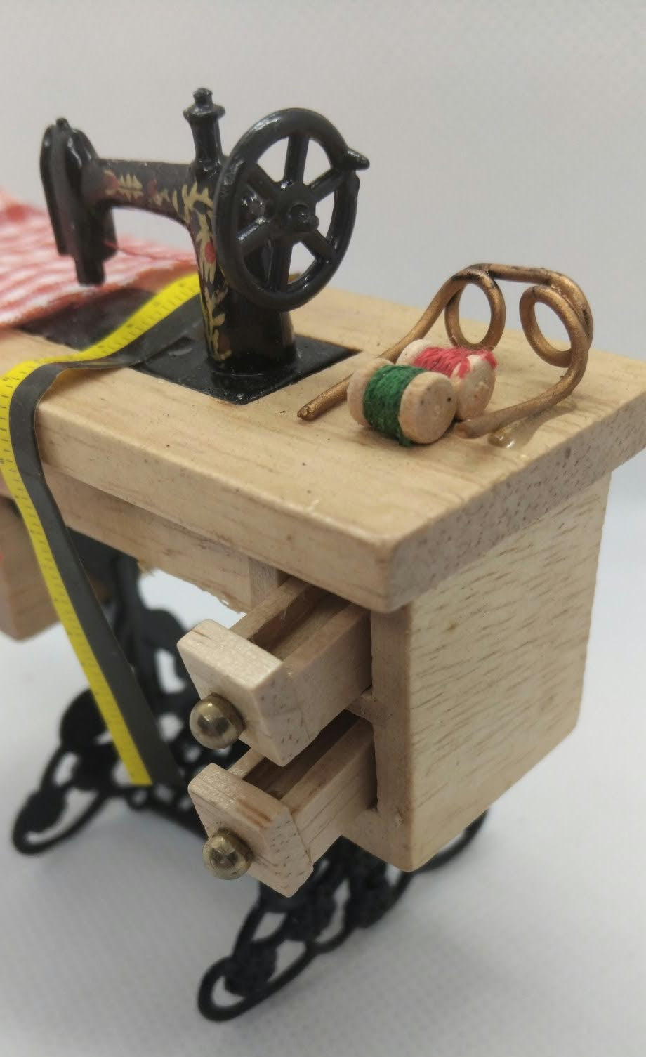 A miniature wooden sewing machine with a light natural wood body, black metal base and wheel, yellow guide tape, and small spool details on a plain white background.