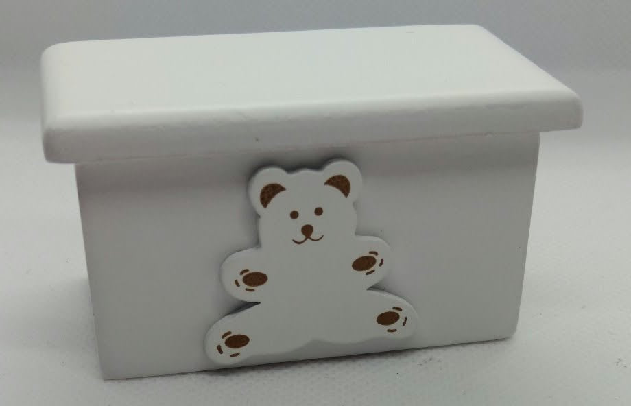 A small white rectangular box with a lid, featuring a white teddy bear charm with brown details on the front, set against a plain light gray background.