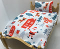 A miniature wooden bed frame with a white Christmas-themed bedding set featuring a Santa Claus print, reindeer, red houses, and 'Ho Ho Ho' text, shown against a plain light background.