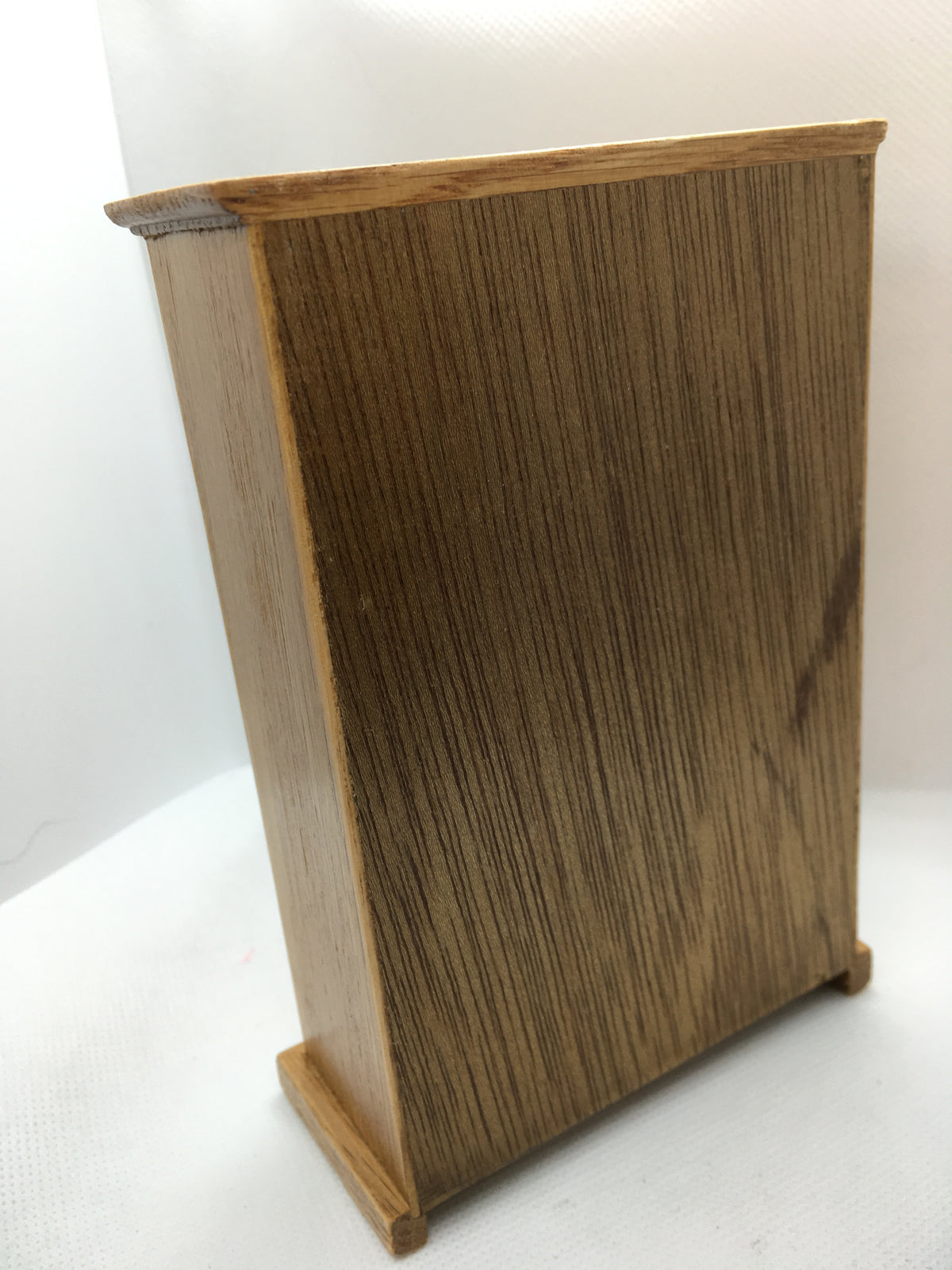 A miniature wooden wardrobe  with a detailed wood grain finish, standing on a white textured surface against a white background.