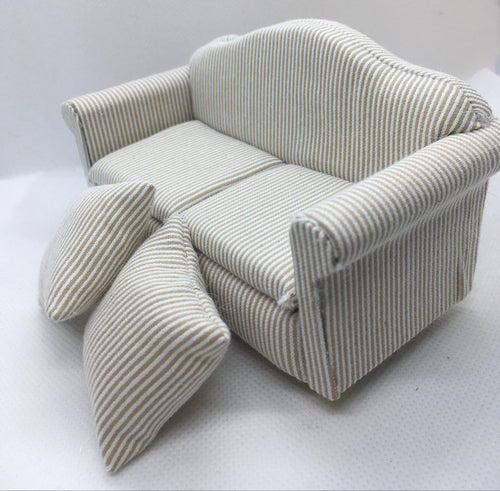 A miniature fabric sofa and two matching pillows, upholstered in a beige and white vertically striped material, set against a plain light gray background.