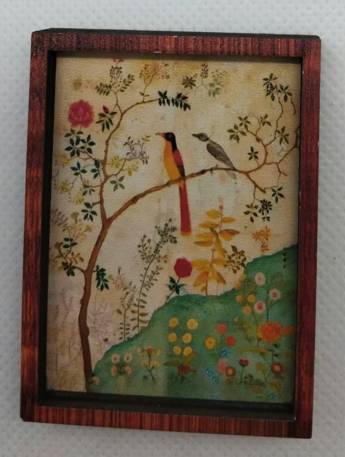 A small framed decorative painting or print showing a bird perched on a flowering tree, with a red-brown wooden frame, photographed against a plain light background.