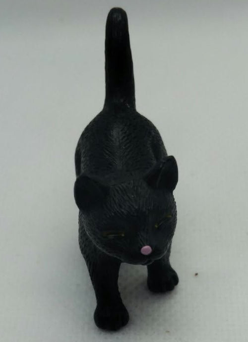 A small black figurine of a cat standing on a white textured surface against a white background.