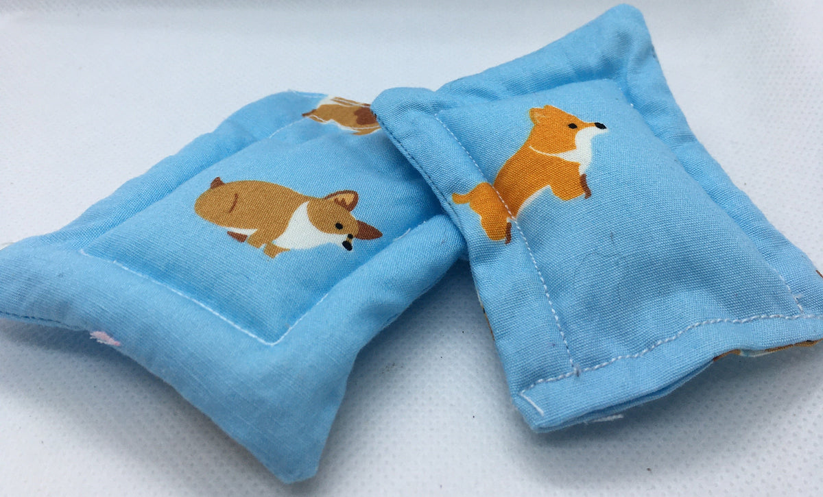 Two small light blue fabric dog beds with printed corgi dog illustrations, photographed on a plain white surface.