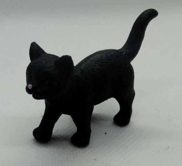 A small black cat figurine standing on a plain light background.