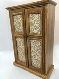 A small 1:12th scale wooden wardrobe with two doors, featuring cream-colored panels with a vintage floral and bird pattern in muted green, red, and brown tones, set against a plain white background.
