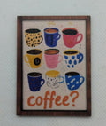 A framed wall art print featuring colorful illustrated coffee mugs and the word 'coffee?' in orange, hung on a light gray textured wall.