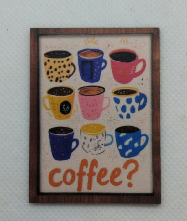 A framed wall art print featuring colorful illustrated coffee mugs and the word 'coffee?' in orange, hung on a light gray textured wall.