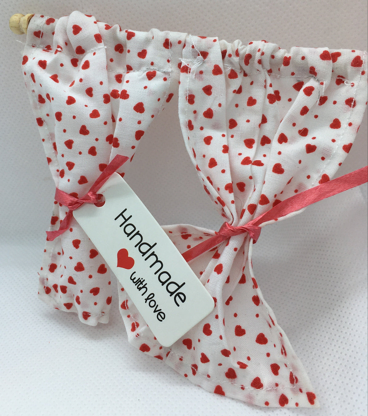 A pair of handmade white fabric curtain panels with a red heart pattern, tied with pink ribbons and a white tag that reads 'Handmade with love'.