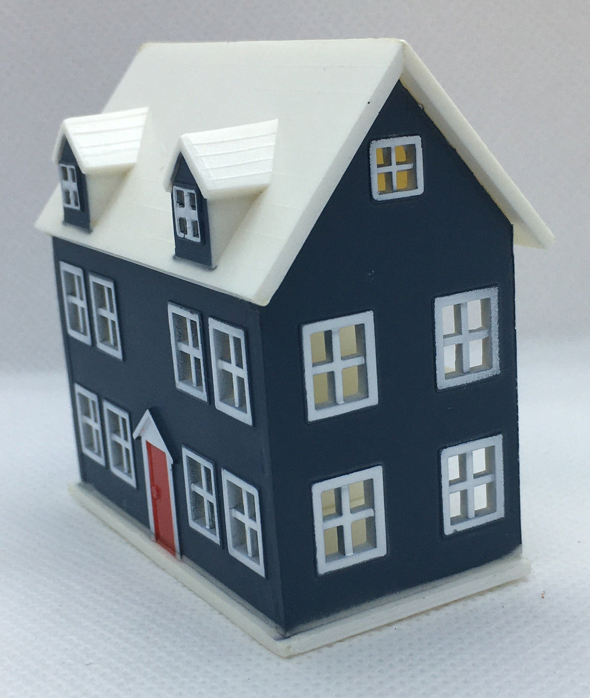 A miniature house-featuring a dark navy blue facade, white roof and trim, and a small red front door, set against a plain light gray background.