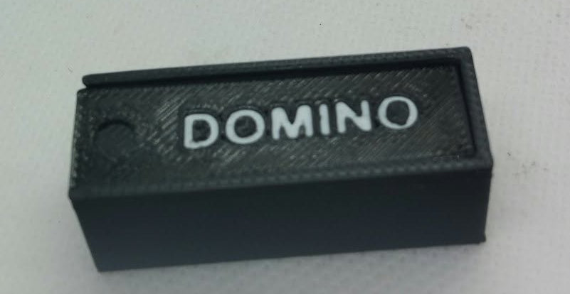 A small black rectangular domino set with the word 'DOMINO' printed in white on the top, photographed on a plain light background.