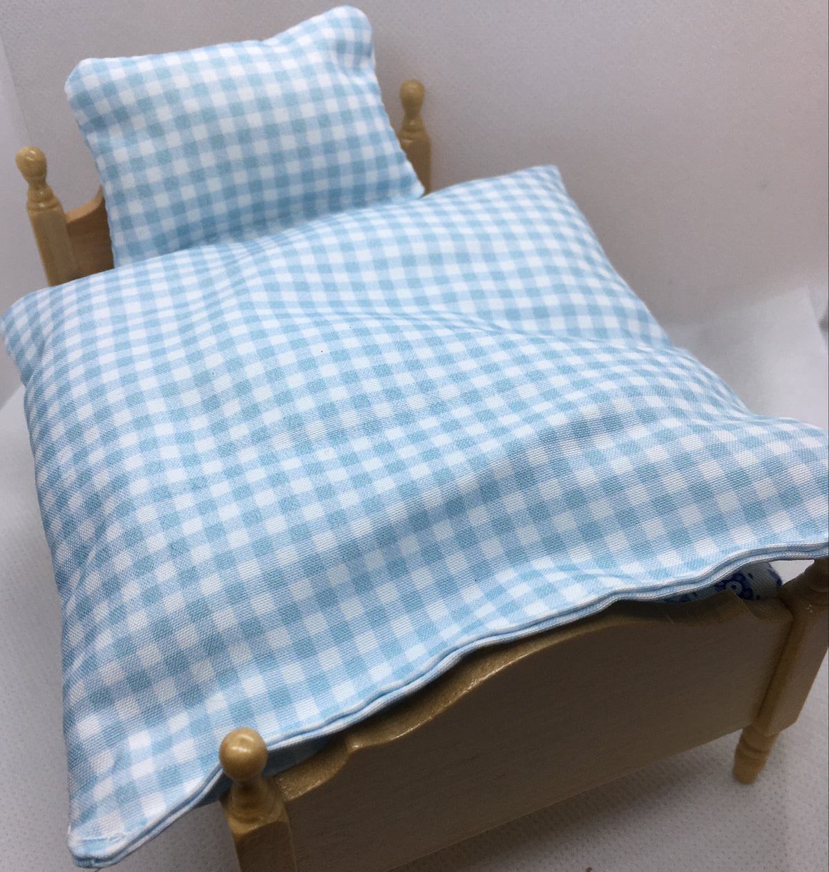 A light blue and white gingham check bedding set, including a duvet cover and matching pillowcase, displayed on a miniature wooden bed frame.