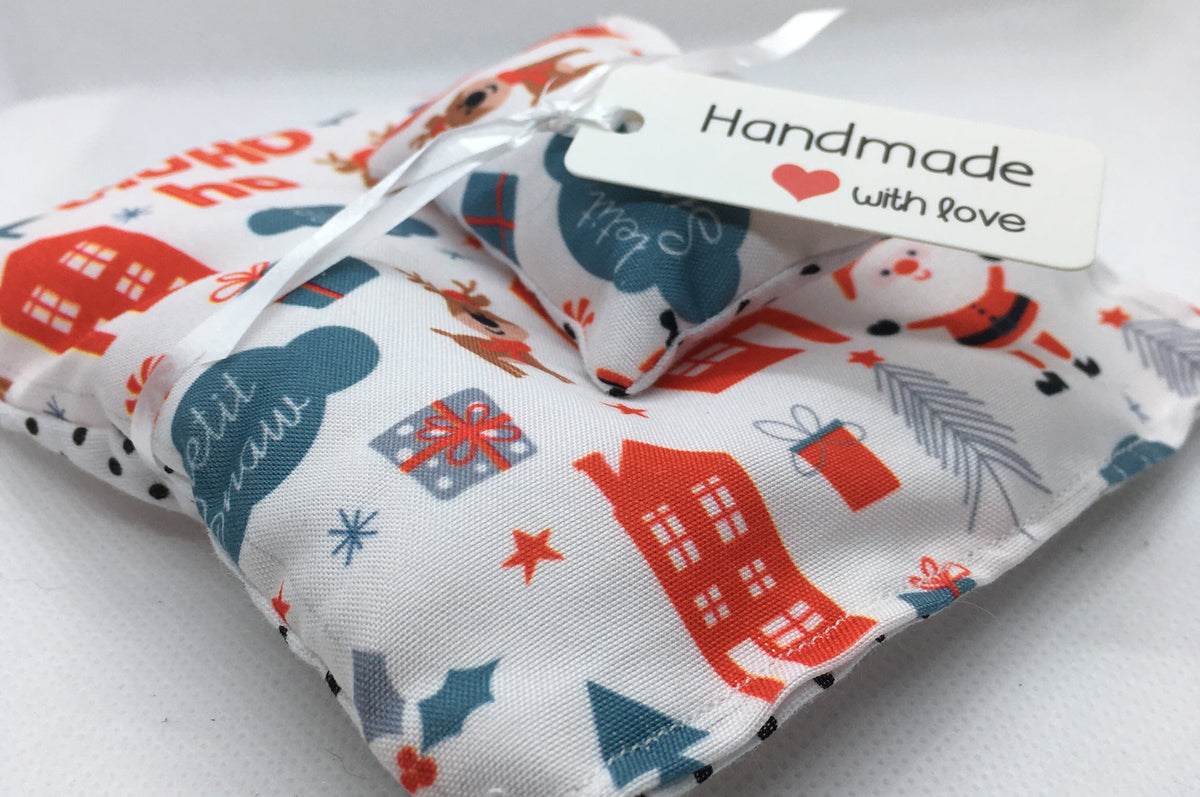 A small handmade duvet set for your dolls house bed with a white background and a festive print in red and blue, tied with a white ribbon and a paper tag that reads 'Handmade with love'.