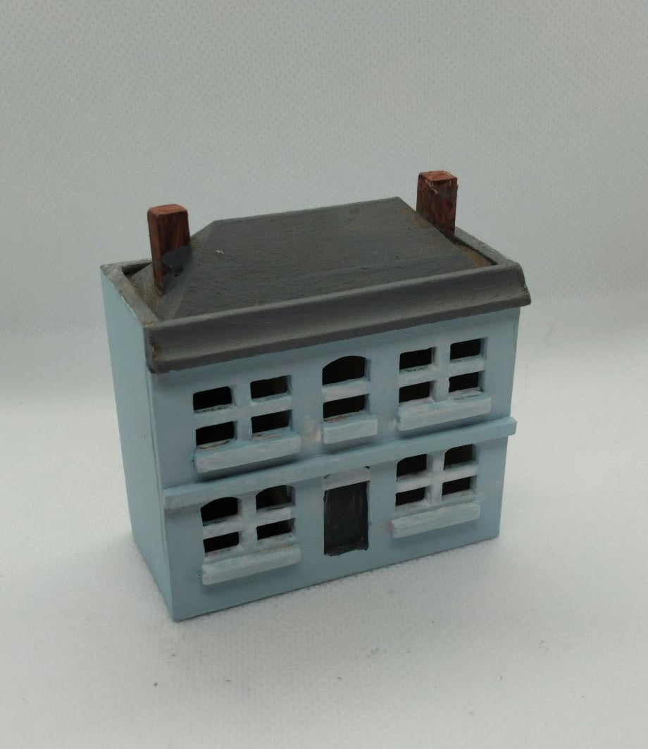A miniature model of a two-story house, featuring a light blue body, a dark gray roof, and brown chimney pots, set against a plain light gray background.