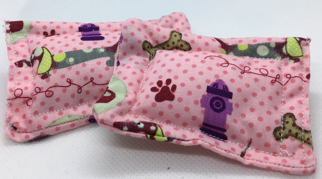 A pink fabric pet accessory,  a small pet bed for 1:12th scale pets, featuring a polka dot pattern with dog toys, paw prints, and a purple fire hydrant, displayed on a white background.
