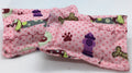 A pink fabric pet accessory,  a small pet bed for 1:12th scale pets, featuring a polka dot pattern with dog toys, paw prints, and a purple fire hydrant, displayed on a white background.