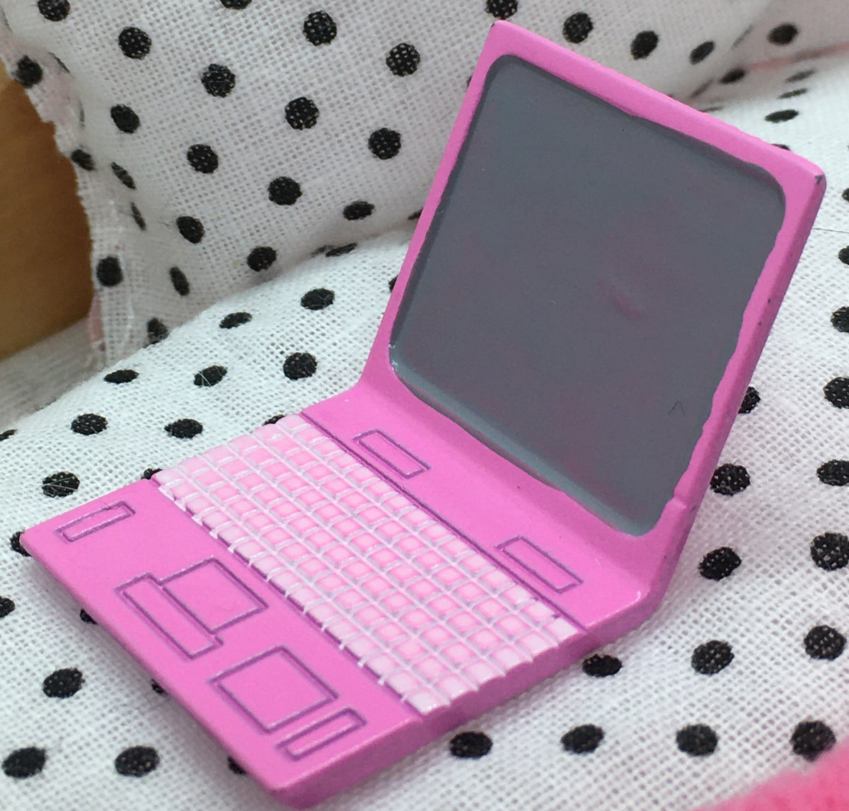 small resin pink laptop on a miniature single bed with white and black polka dots duvet set. 
