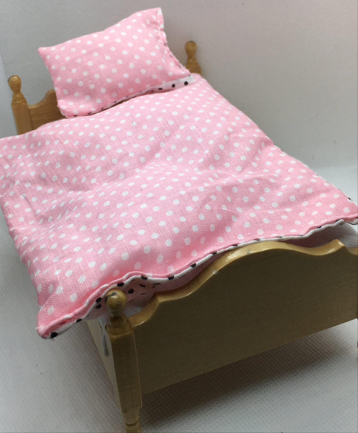 Pink bedding set with white polka dots, including a duvet cover and matching pillow, displayed on a miniature wooden bed frame.