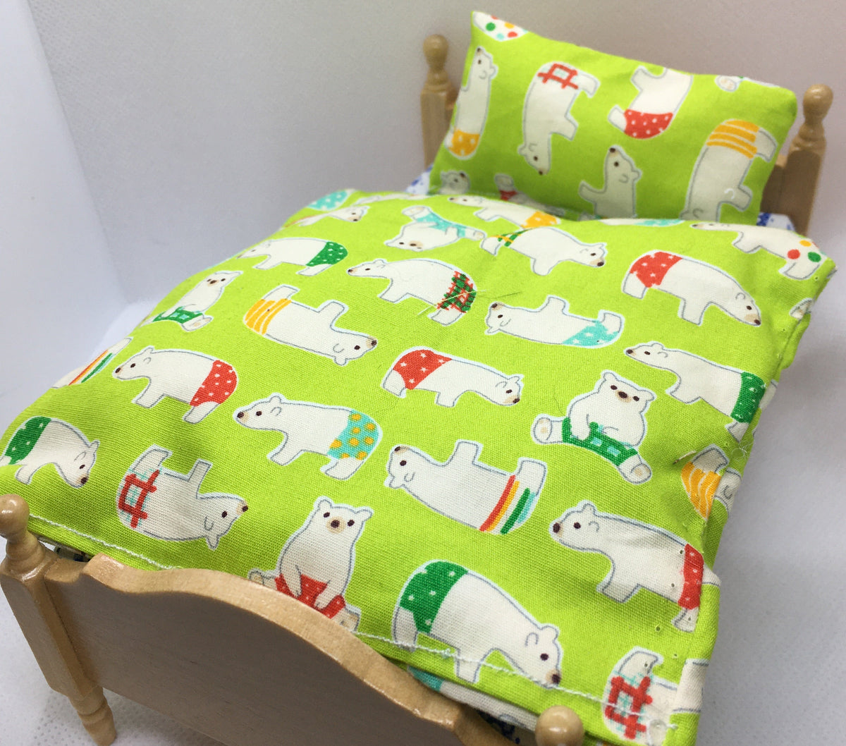 A miniature wooden bed frame shown with a bright lime green bedding set featuring a white polar bear pattern with red, green, and orange accents, photographed against a plain white background.