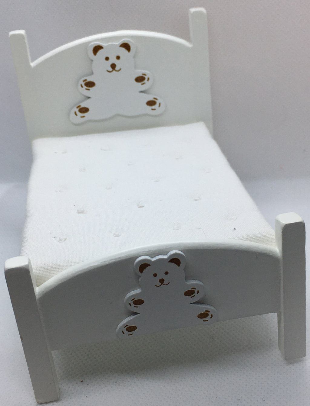 A miniature white dollhouse bed featuring decorative bear cutouts on the headboard and footboard, set against a plain light background.