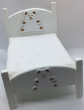 A miniature white dollhouse bed featuring decorative bear cutouts on the headboard and footboard, set against a plain light background.