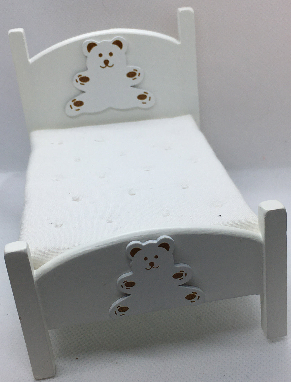 A miniature white dollhouse bed featuring decorative bear cutouts on the headboard and footboard, set against a plain light background.